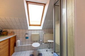 Une salle de bain moderne avec un puits de lumière, des toilettes, un radiateur et un petit tabouret.