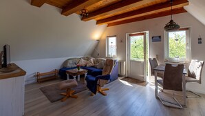 Una habitación con techo de madera, un sofá, una mesa de comedor con sillas y una ventana con vistas al verdor.