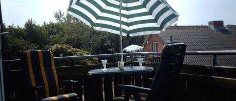 Un balcón con dos sillas a rayas, una mesa y un paraguas a rayas verde y blanco.