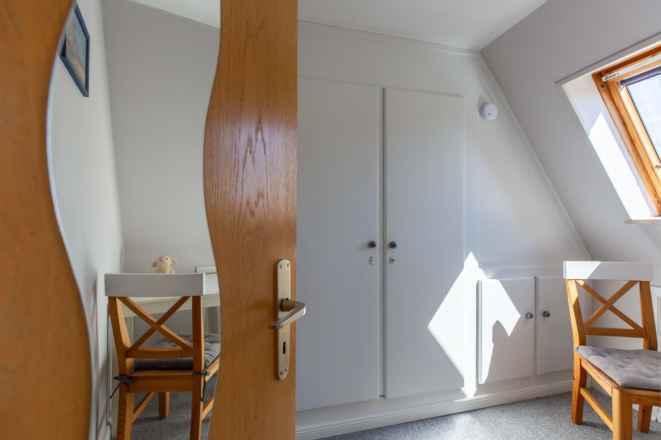 Une pièce avec un plafond en pente, une armoire, deux chaises en bois et une petite table.