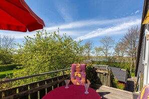 A deck with a red umbrella, a chair with a floral cushion, and a view of a lake.