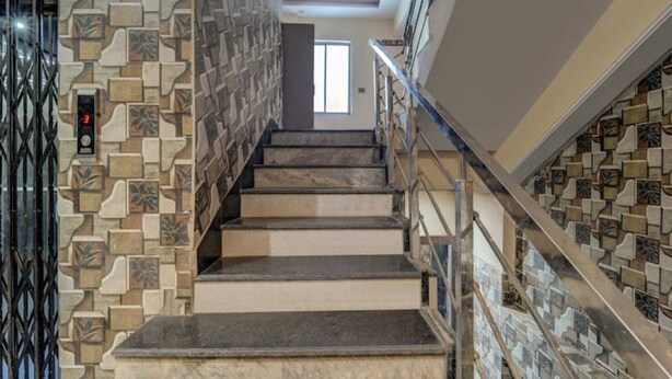 A staircase with stone wall panels and a metal railing. - Raj Palace Guest House (Patna)