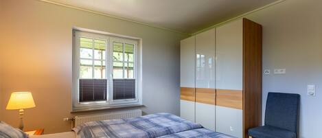 A bedroom with two beds, a window with blinds, a chair, and a wardrobe.