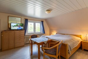 A bedroom with a bed, a desk with a chair, a television, and a wardrobe.