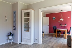 A room with a white cabinet, a dining table with chairs, a red wall, and a hanging light fixture.