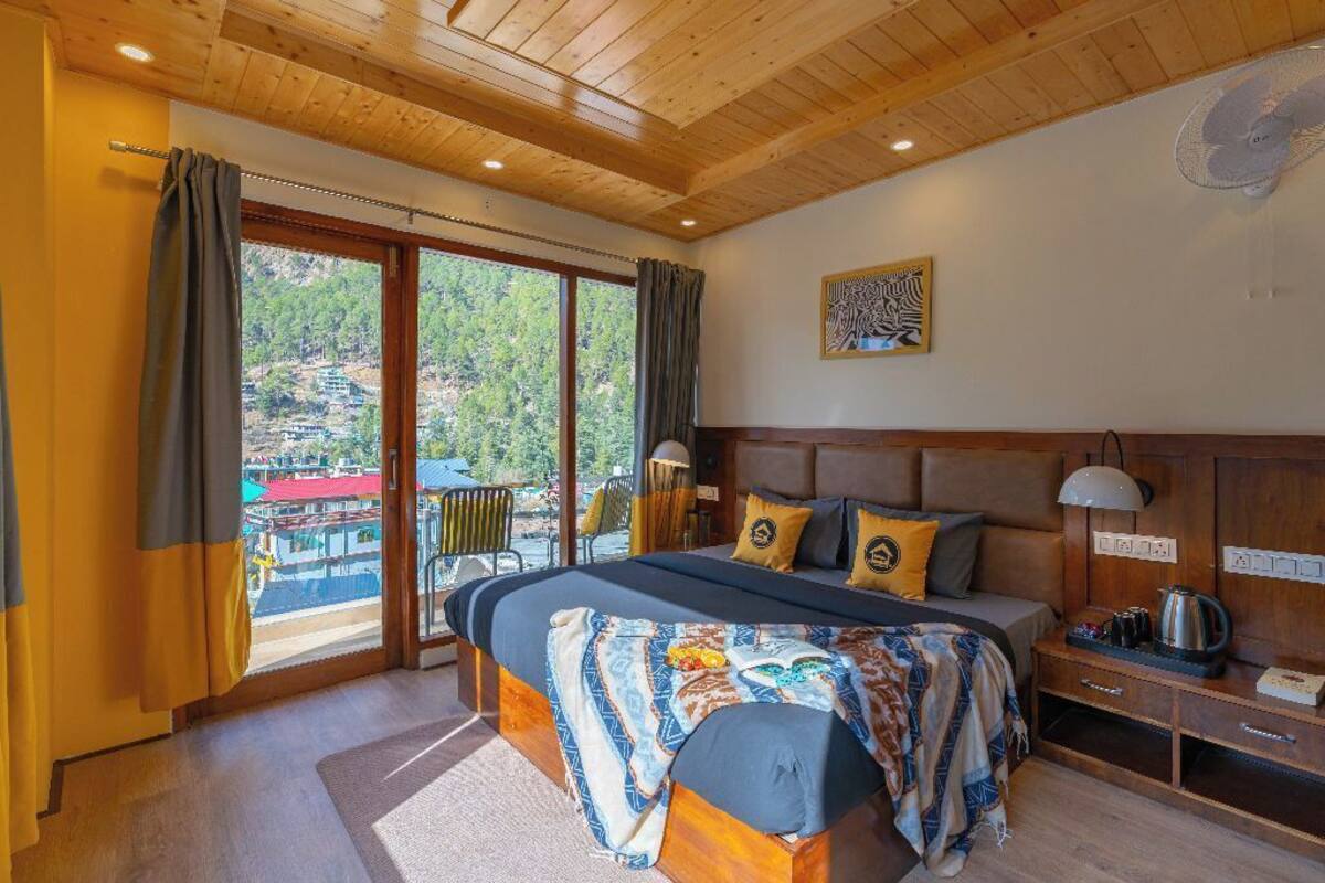 Une chambre dotée d’un grand lit, d’une tête de lit en bois et donnant sur un balcon aménagé avec des sièges d’extérieur.