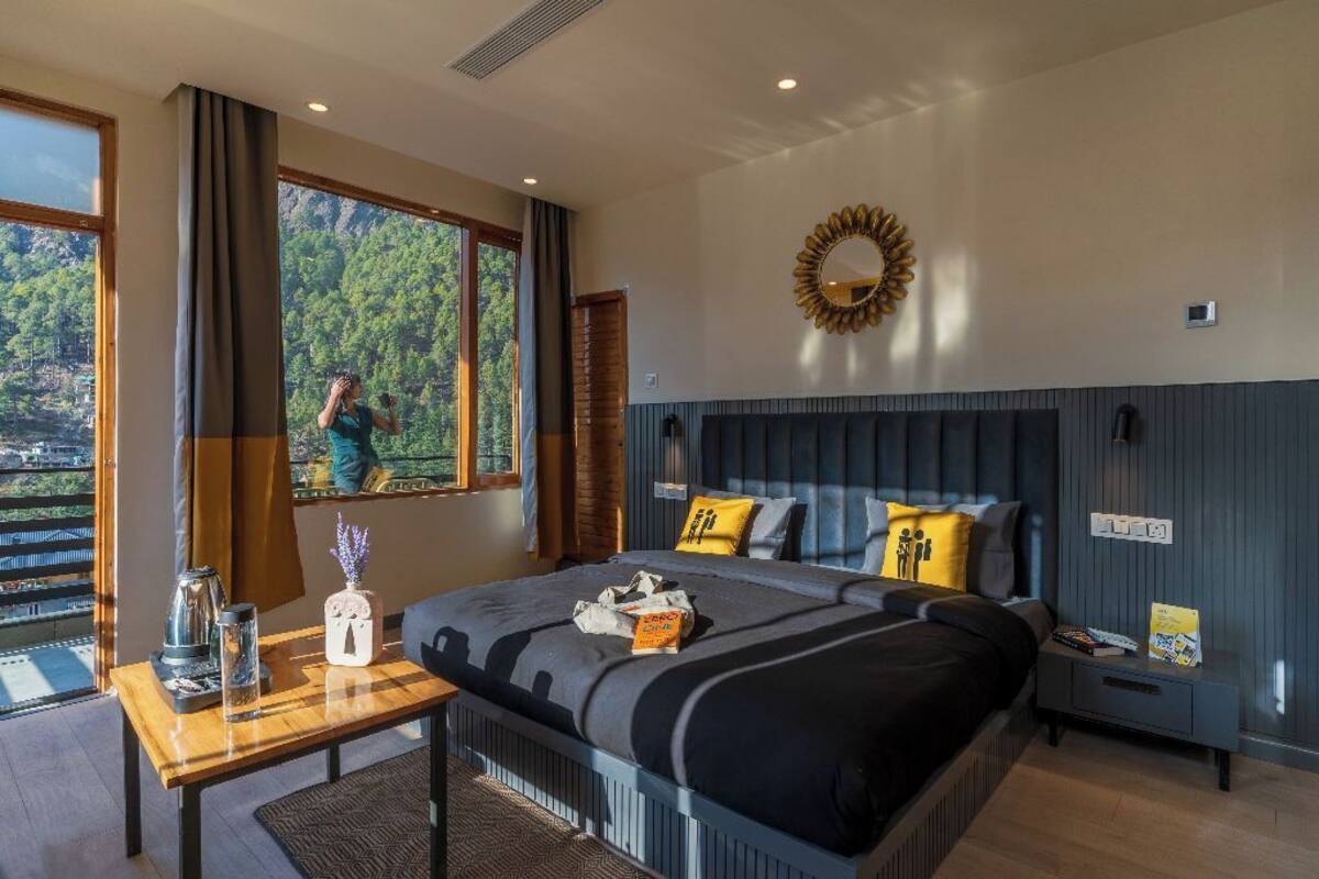 Une chambre moderne avec un grand lit, une table de chevet, une vue sur l’extérieur et un miroir décoratif au mur.