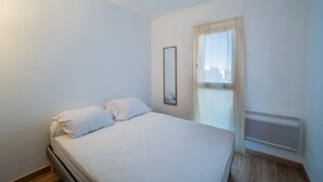 Un dormitori amb un llit, una finestra amb cortines, un calefactor fixat a la paret i un mirall.
