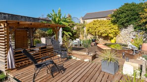 A wooden deck with outdoor furniture, a pergola, and a stone wall.