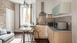 A modern kitchen with a brick wall, a dining area with a sofa, and a large window. - Le Petit 18 - T2 proche de la gare (Rennes)