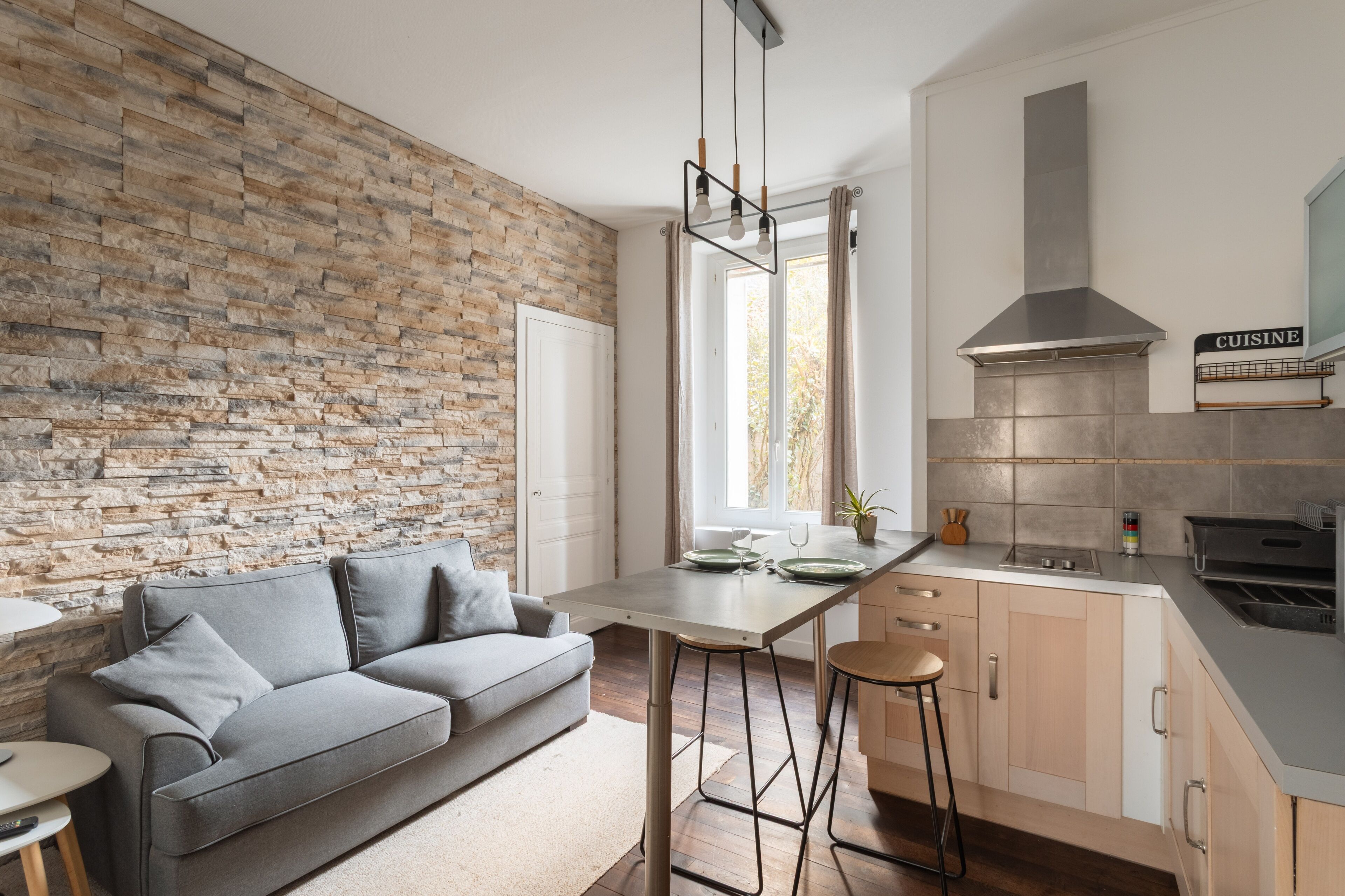 Une cuisine moderne avec un mur en pierre, un canapé gris et un coin bar.