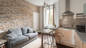 A modern kitchen with a stone wall, a grey sofa, and a bar area. - Le Petit 18 - T2 proche de la gare (Rennes)