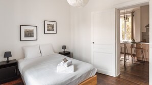 A bedroom with a bed, bedside tables, framed pictures, and a door leading to a kitchen area. - Le Petit 18 - T2 proche de la gare (Rennes)