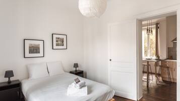 Une chambre à coucher comprenant un lit, des tables de chevet, des tableaux encadrés et une porte donnant sur un coin cuisine.