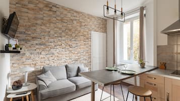 Une cuisine moderne avec un mur en pierre, un canapé gris et un coin repas avec des tabourets.