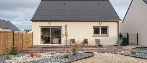 A modern house with a patio, two chairs, and a small garden area.