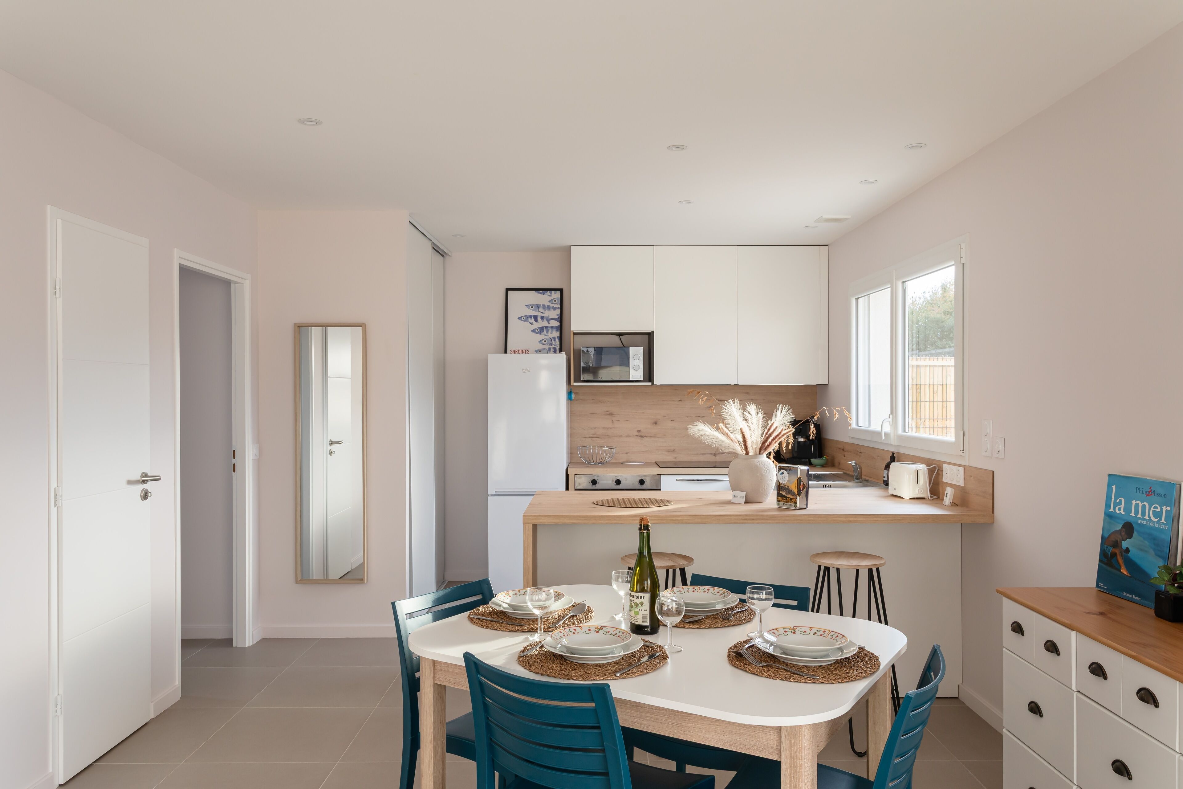 A modern kitchen with white cabinets, a wooden countertop, and a dining area with a white table and blue chairs.