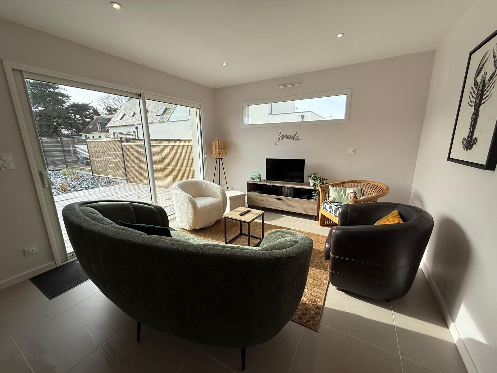 A modern living room with a sofa, armchairs, a TV, and a bookshelf.