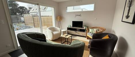 A modern living room with a sofa, armchairs, a TV, and a bookshelf.