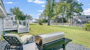 Un giardino sul retro con un barbecue, un'area salotto coperta e un patio che si affaccia su uno specchio d'acqua.