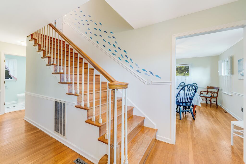 A staircase with wooden steps and white railings, leading to a room with a dining area.