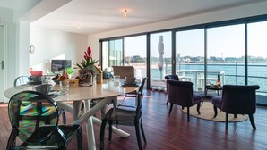 A modern dining area with a large table, chairs, and a view of the sea.
