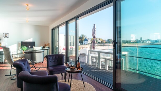 A modern living room with a large glass door leading to a balcony with a view of the sea.