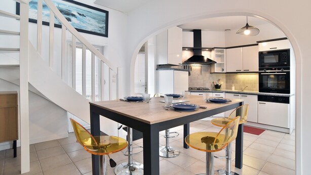 Una cocina moderna con armarios blancos, un microondas negro y un comedor con una mesa de madera y sillas amarillas.