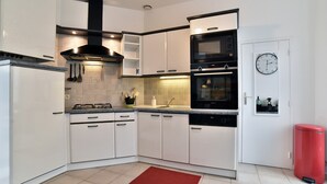 Una cocina moderna con armarios blancos, una campana extractora negra, horno empotrado y un cubo de basura rojo.