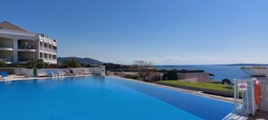 Una piscina con sillones de descanso, un edificio con balcones y vista al mar.