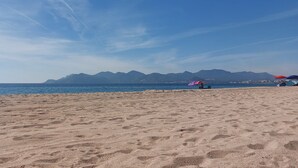 Una playa con arena, agua y montañas a lo lejos.