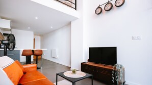 Una sala moderna con un sofá, un televisor, una mesita y una escalera que sube a un nivel superior.