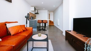 Una sala de estar moderna con un sofá de cuero, una mesa de centro, un televisor y una cocina al fondo.