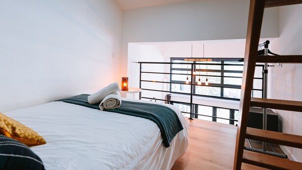 Un dormitorio con cama, una escalera de madera, un escritorio y una ventana con vistas.