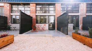 A modern building with a brick facade, large windows, and a gravel courtyard with outdoor seating.