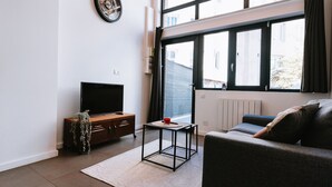 A modern living room with a flat-screen TV, a wooden cabinet, a small table with a red cup, and a sofa with cushions.