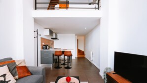 A modern living room with a grey sofa, a coffee table with a red object, and a TV on a wooden stand.