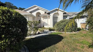 A residential house with a well-maintained lawn, a curved driveway, and a variety of shrubs and plants.