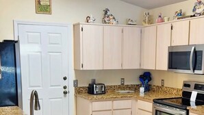 A compact kitchen with a central island, two bar stools, a microwave, a toaster, and a refrigerator.