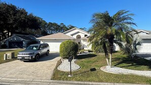 A residential driveway with a parked SUV, a mailbox, and a well-maintained lawn with a palm tree.