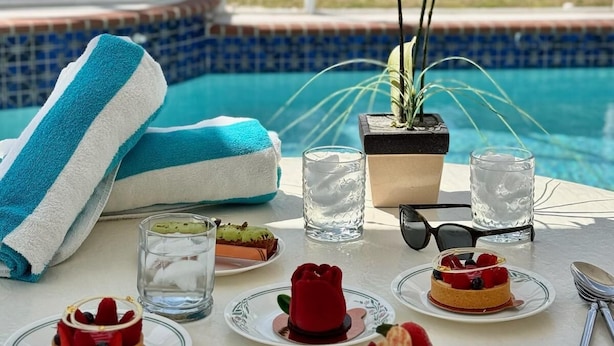 A poolside table with desserts, a potted orchid, and a blue and white towel.