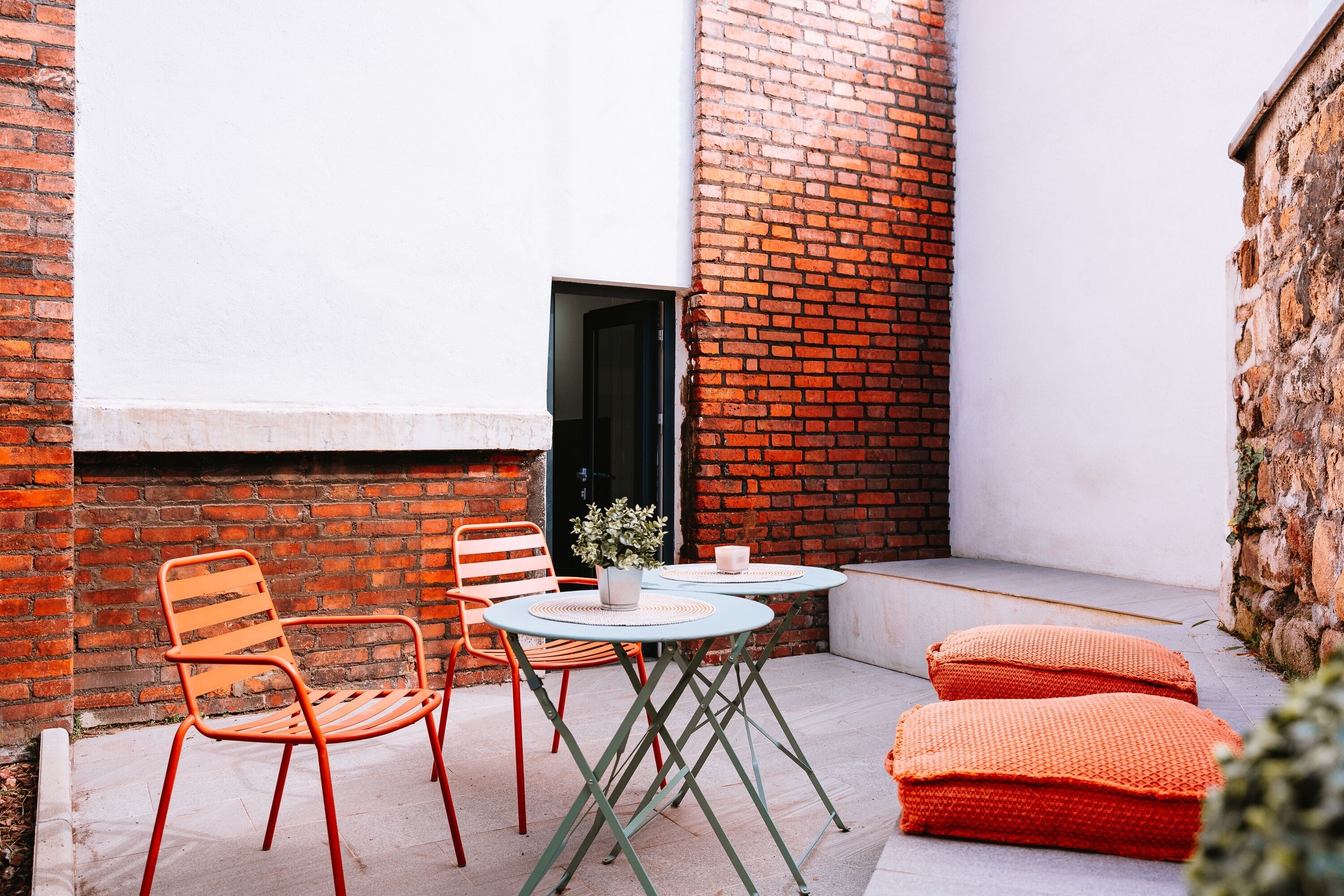 Un petit espace extérieur aménagé avec une table et des chaises, un pot de fleurs et un mur en briques.