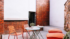 A small outdoor seating area with a table and chairs, a potted plant, and a brick wall.