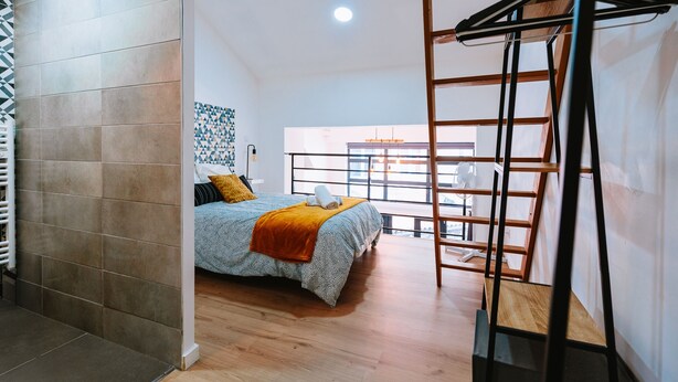 A bedroom with a bed, a wooden ladder, and a window with a view.