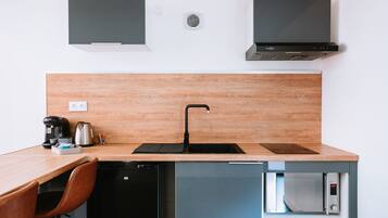 Une cuisine compacte dotée d’un plan de travail en bois, d’un évier noir, d’un four à micro-ondes encastré et d’un lave-vaisselle.