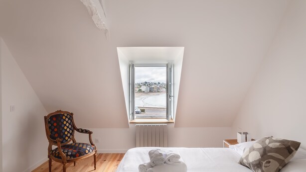 A bedroom with a bed, a chair, a window, and a radiator.