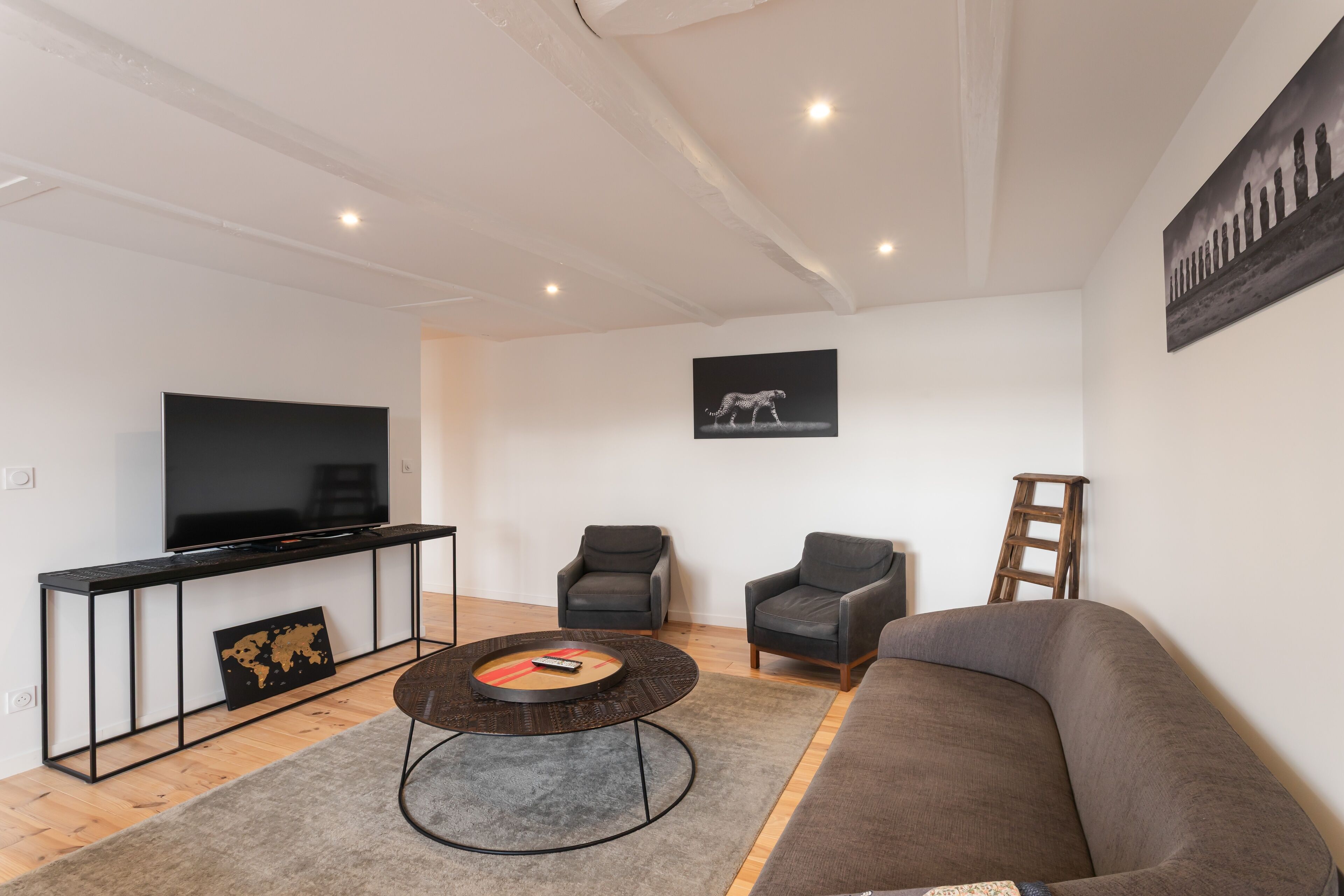 Ein modernes Wohnzimmer mit Flachbildfernseher, zwei Sesseln, einer Couch, einem Couchtisch und einer Weltkarte als Wandbild.