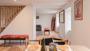 A dining area with a wooden table set for two, a bottle of wine, and a framed picture on the wall.
