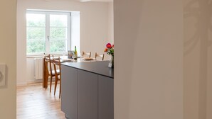A modern kitchen with a central island, wooden chairs, a window with a view, and a radiator.