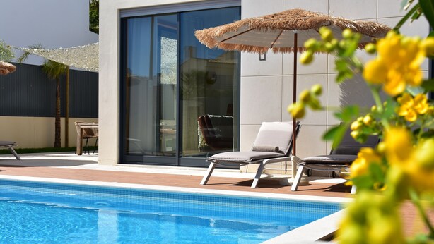 Une piscine avec des chaises longues et un parasol en chaume.